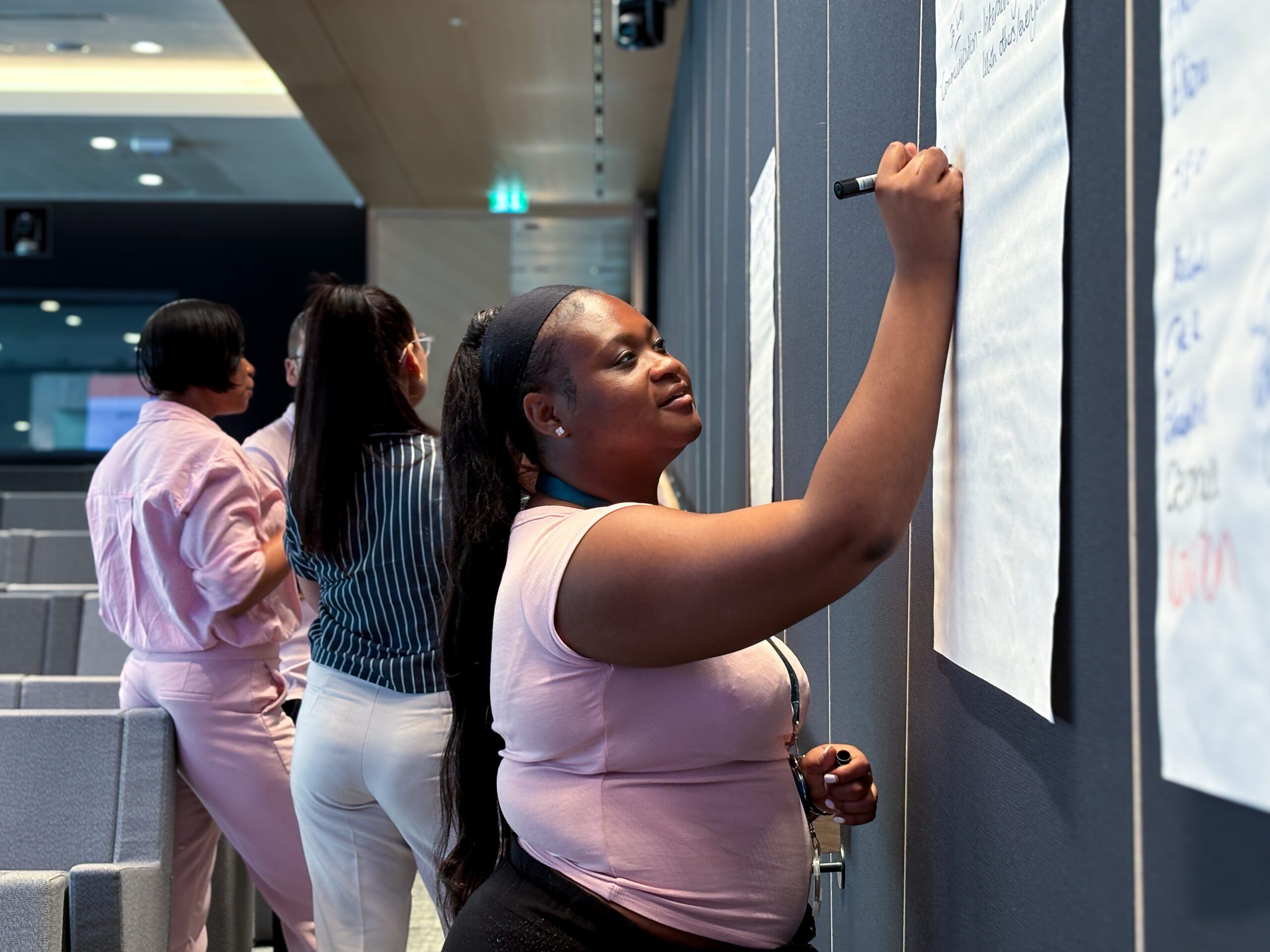Person wearing pink tshirt writing on a poster on wall
